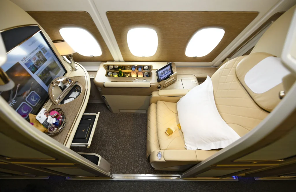 Emirates A380 First Class private suite with lie-flat leather seat, mini bar, vanity mirror, and in-flight entertainment screen.
