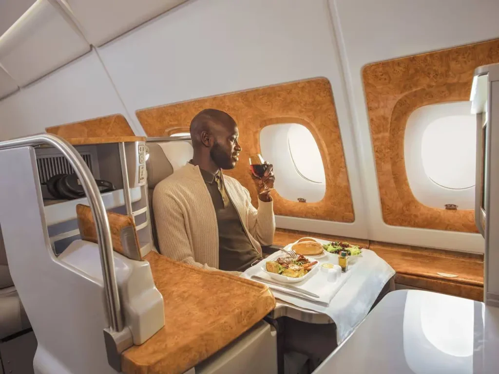 Passenger enjoying gourmet lunch and wine in Emirates Business Class cabin with personalized in-flight dining service.