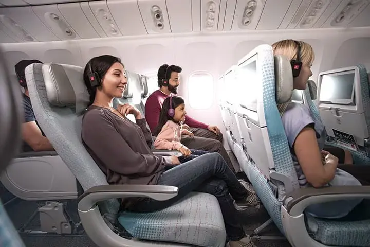 Families enjoying in-flight entertainment screens in Emirates A380 Economy Class cabin.